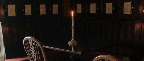 Un restaurante con poca luz, con cabinas de madera, una mesa con vela y pizarras con la carta en la pared.