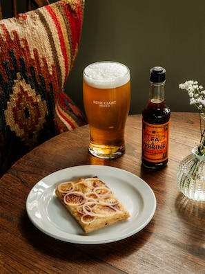 A table with a glass of beer, a bottle of Lea & Perrins sauce, and a slice of onion tart on a plate.