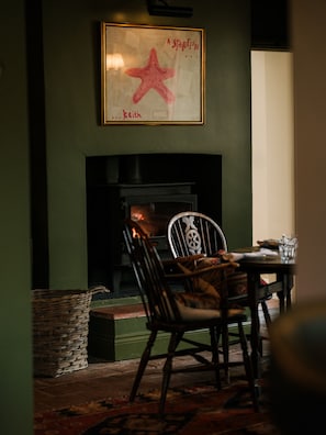 A room with a fireplace, a framed artwork, a chair, and a table.