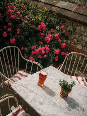 A marble table with a glass of beer, two chairs, and a potted plant.