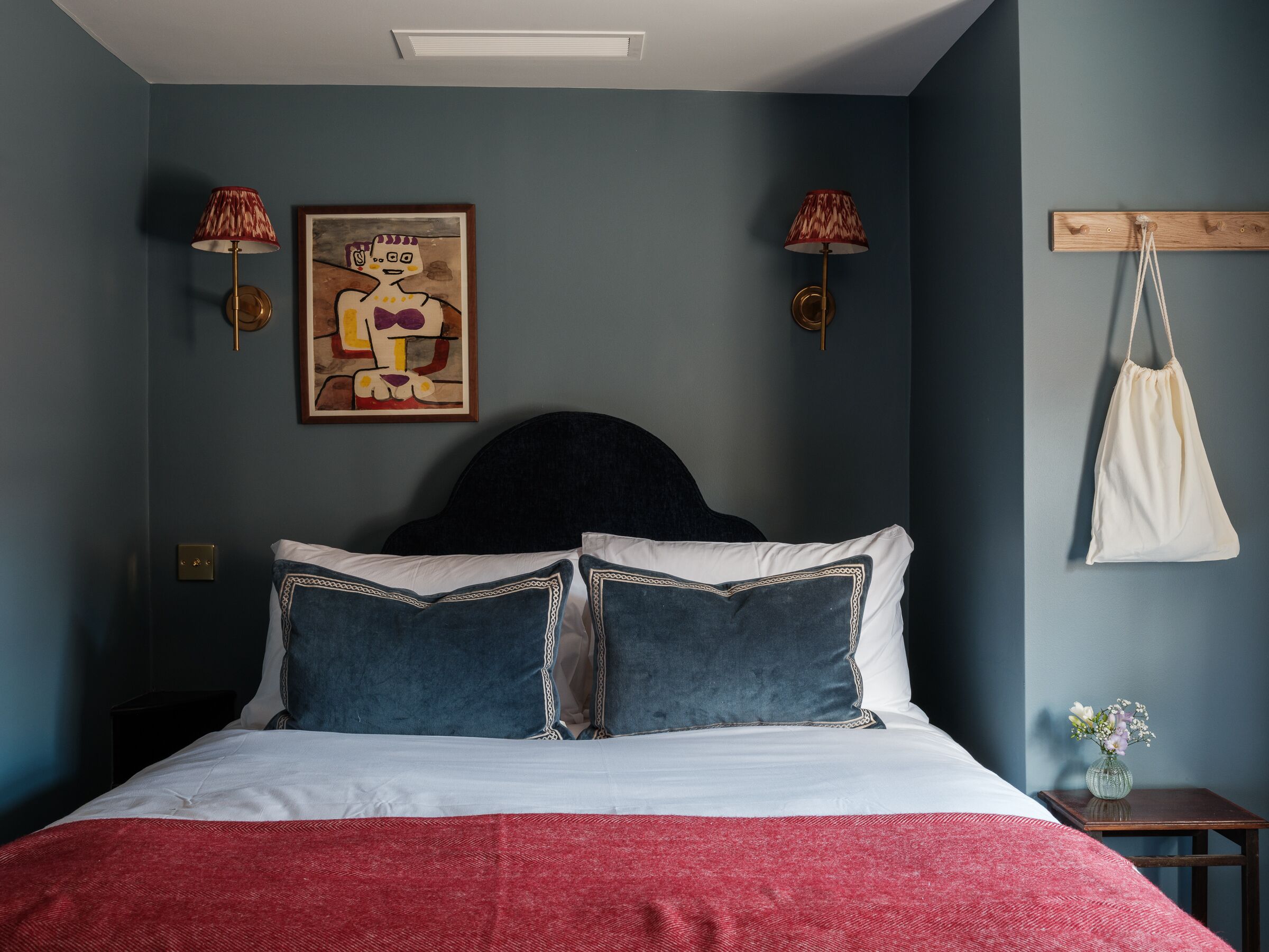 Una camera da letto con un letto, due lampade a parete, un quadro e una borsa appesa.