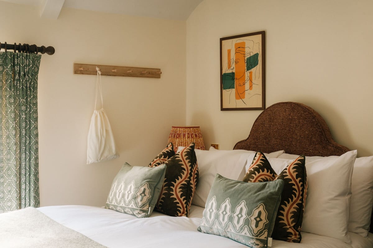 A bed with patterned pillows, a headboard, a hanging bag, and a framed artwork on the wall.