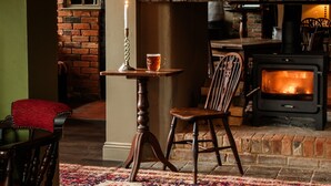A cozy interior with a brick fireplace, a table with a candle, and a menu on the wall. - The Great Decoy (Hurstbourne Tarrant)