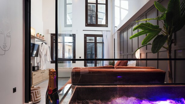 A modern living room with a glass partition, a sofa, a plant, and a bottle of champagne.