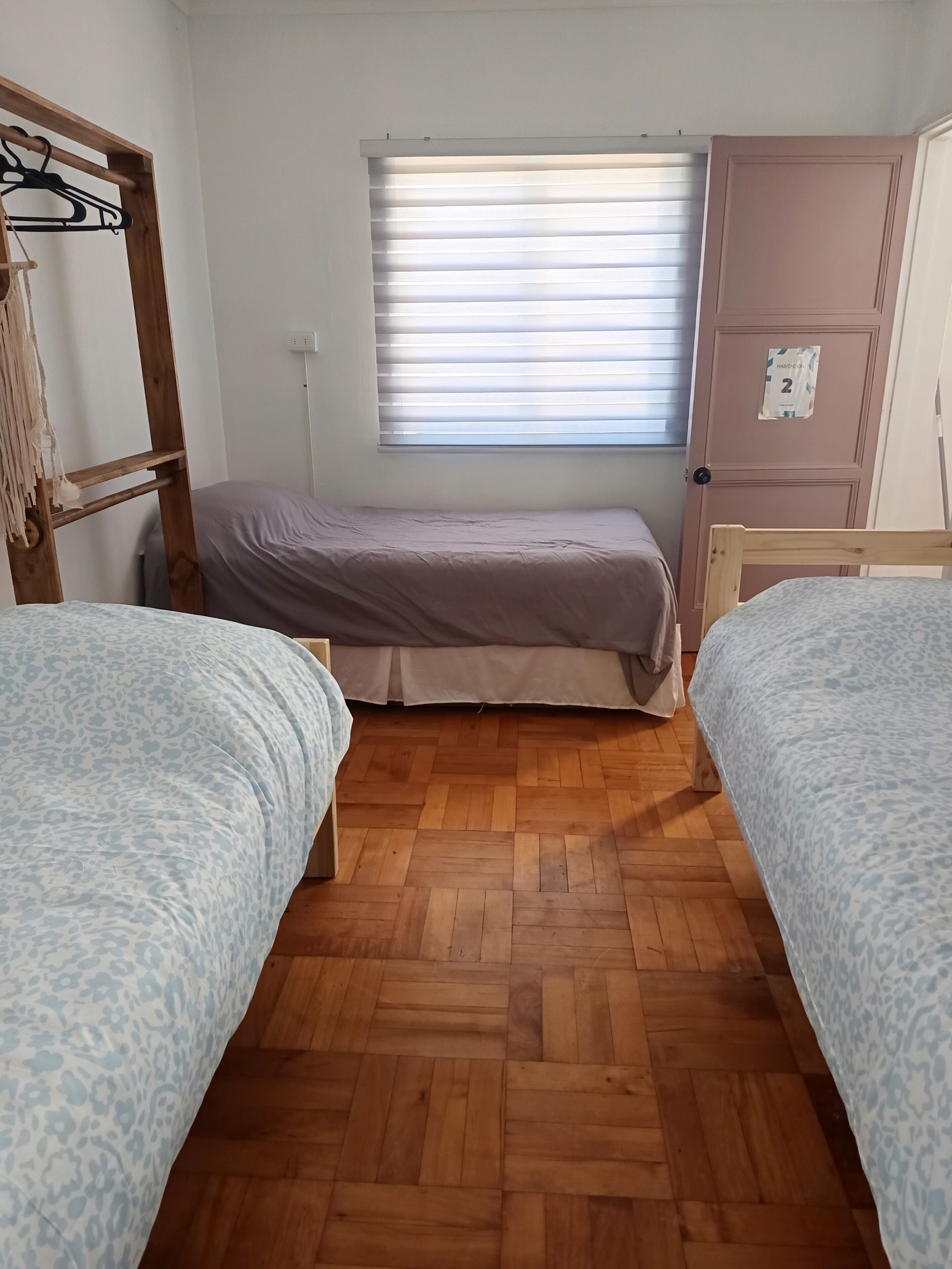 Un dormitorio con dos camas, una ventana con persianas, un armario y suelo de madera.
