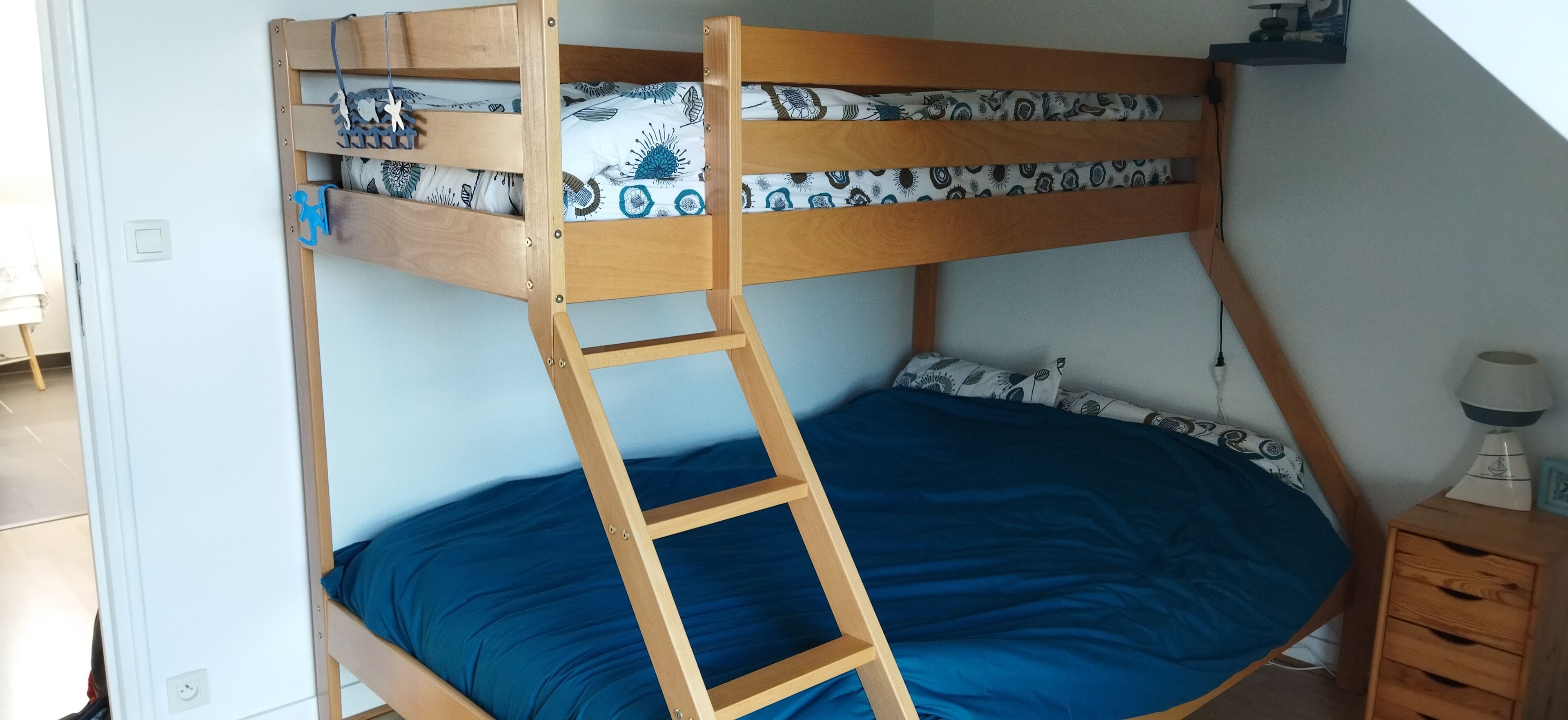 Una cama individual superpuesta con una escalera de madera, un colchón azul y una mesita de noche con una lámpara.