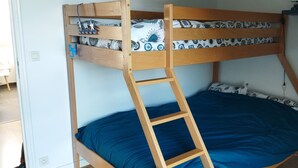 Ein Stockbett mit Holzleiter, einer blauen Matratze und einem Nachttisch mit Lampe.