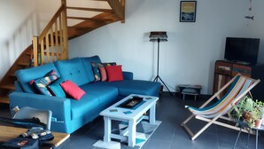 Ein Wohnzimmer mit einem blauen Sofa, einem kleinen Couchtisch, einer gestreiften Hängematte, einem Fernseher und einer Treppe.