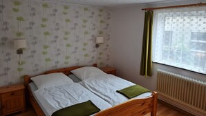Ein Schlafzimmer mit einem hölzernen Bett, zwei Nachttischen, einem Heizkörper und blumigem Tapetenmuster.