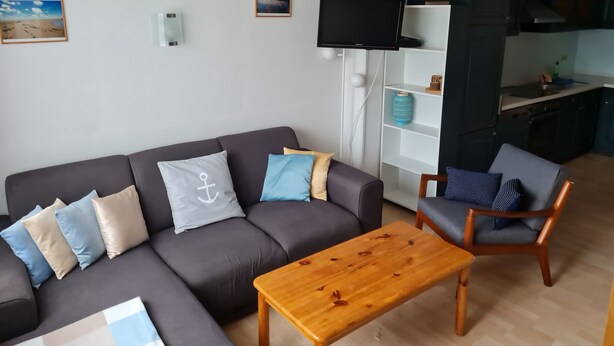 Un salon comprenant un canapé, une table basse en bois, un téléviseur et un coin cuisine avec des placards et un évier.