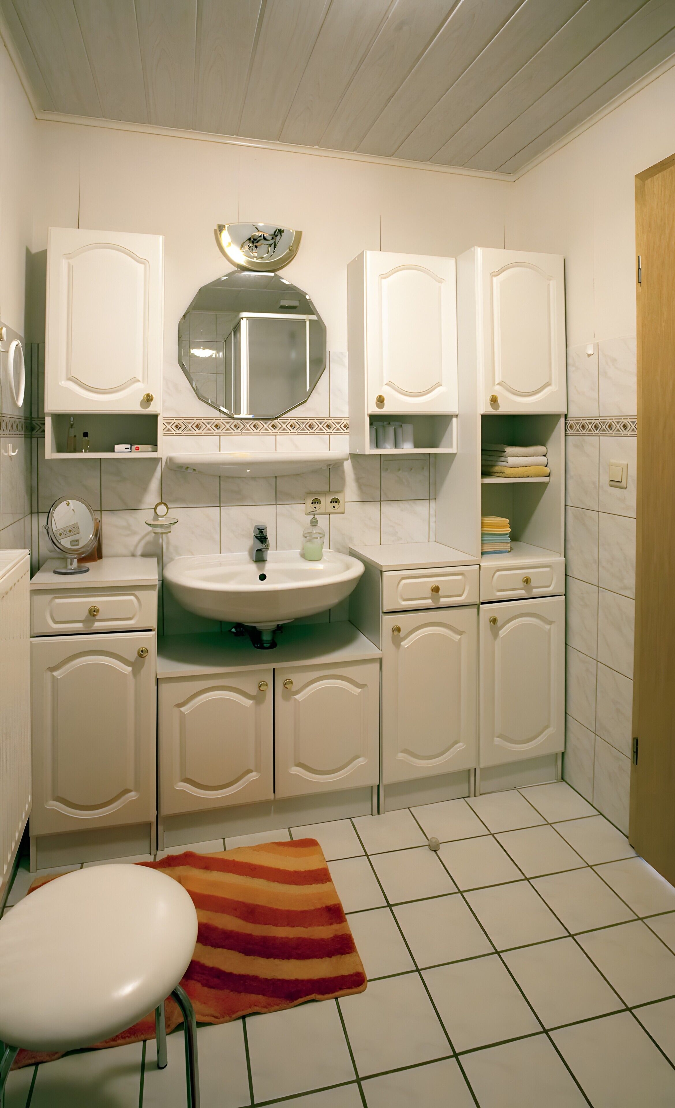Une salle de bain avec un lavabo, un miroir, des placards et un tapis à rayures.