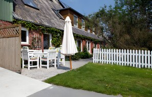 A house with a white picket fence, a patio with a table and chairs, and a white umbrella. - Apartment 'Fewo Mirja' with Shared Terrace, Shared Garden and Wi-Fi (Pellworm)