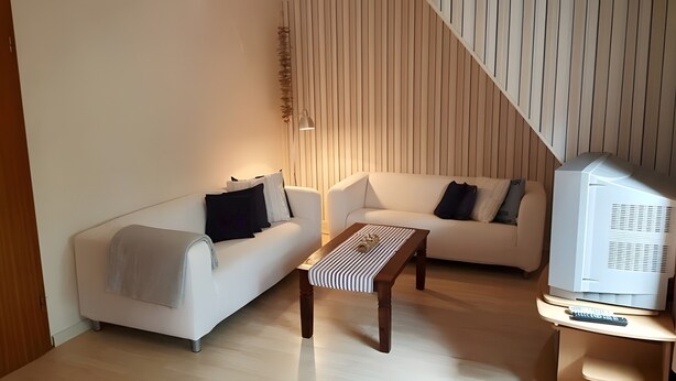Ein modernes Wohnzimmer mit zwei weißen Sofas, einem Holztisch und einem Fernseher auf einem Standfuß.