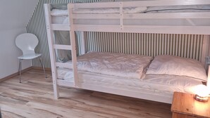 Ein Stockbett mit Holzrahmen, ein weißer Stuhl und ein Nachttisch mit Lampe.