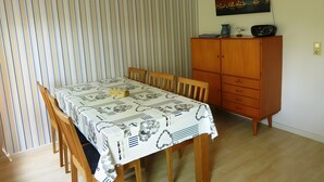 Ein Essbereich mit gestreifter Tapete, einem Tisch mit gemustertem Tischläufer, Holzsesseln, einem Holzschrank und einem Stadtbild an der Wand.