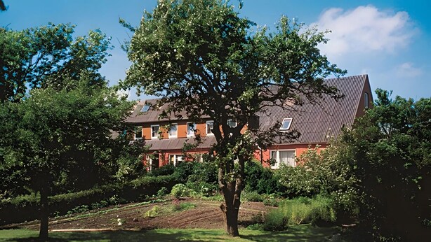 Een huis met een schuin dak, omringd door een verzorgde tuin en bomen.