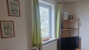 Een kamer met een radiator, een houten stoel, een televisie op een standaard en ingelijste foto's aan de muur.