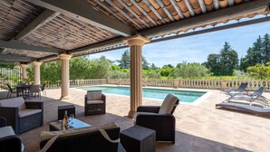Un patio exterior con mobiliario de mimbre, una piscina y una pérgola.