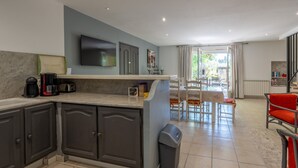 Una cocina moderna con armarios oscuros, una encimera, un televisor y un comedor con mesa y sillas.