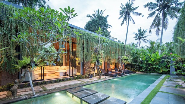 Uma área moderna com piscina ao ar livre, espaço de descanso, rodeada por vegetação exuberante e palmeiras.