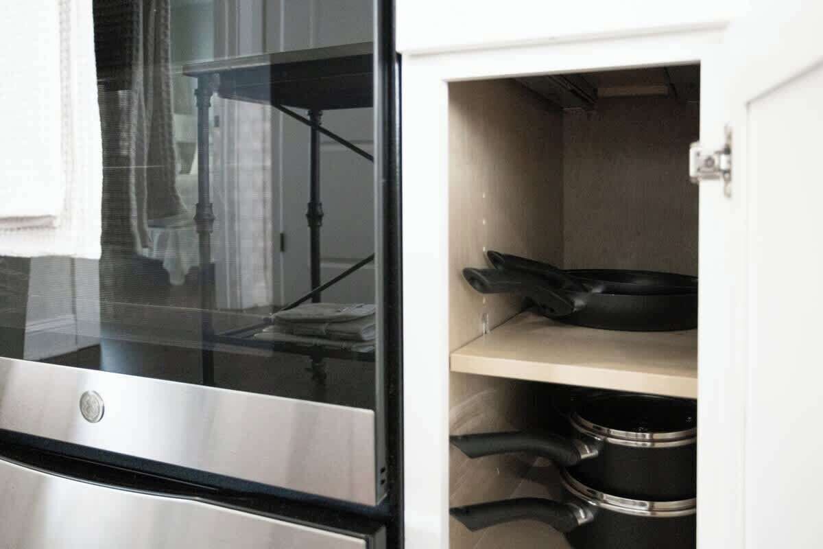 A kitchen with stainless steel appliances, including an oven and a microwave. There is a window with a view of a curtain and a metal rack.