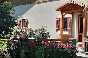 Ein Gebäude mit einer Holzpergola, einem Holzzaun und verschiedenen Kübelpflanzen und Blumen.