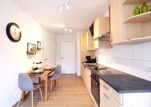 Una cocina moderna con armarios de madera, una encimera negra y un comedor con dos sillas y una mesa.
