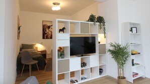 Una sala de estar moderna con un televisor de pantalla plana, una estantería, una silla, una cama y una planta en maceta.