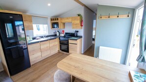 A modern kitchen with wooden cabinets, a black refrigerator, a microwave, and a stove. - MP416 Parkdean Resorts Camber Sands (Camber)