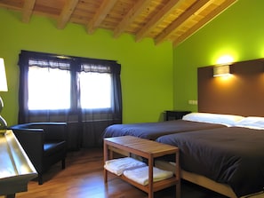 Una habitación con cama, escritorio, silla, una mesita y una ventana con cortinas.