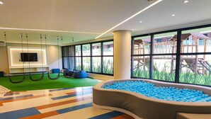 A modern indoor play area with a ball pit, hanging swings, and a TV screen. - Falésia Alliance (João Pessoa)