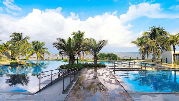 A pool area with palm trees and a view of the sea. - Falésia Alliance (João Pessoa)