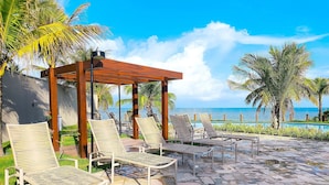A poolside area with lounge chairs and a pergola overlooking a pool and ocean view. - Falésia Alliance (João Pessoa)