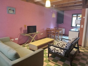 A living room with a sofa, a TV on a stand, a dining table with chairs, and a kitchen area in the background. - Country House 'Villabamba 1' with Mountain Views, Shared Terrace and Wi-Fi (Valdeavellano de Tera)