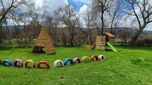 Une aire de jeux avec des structures d’escalade et un toboggan, entourée d’arbres et d’une pelouse.