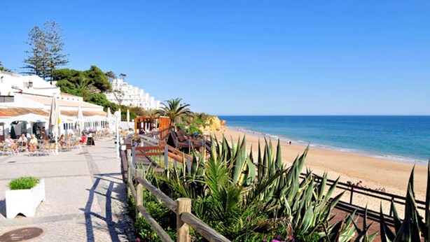 Un paseo marítimo con playa, valla de madera y zonas de estar al aire libre.