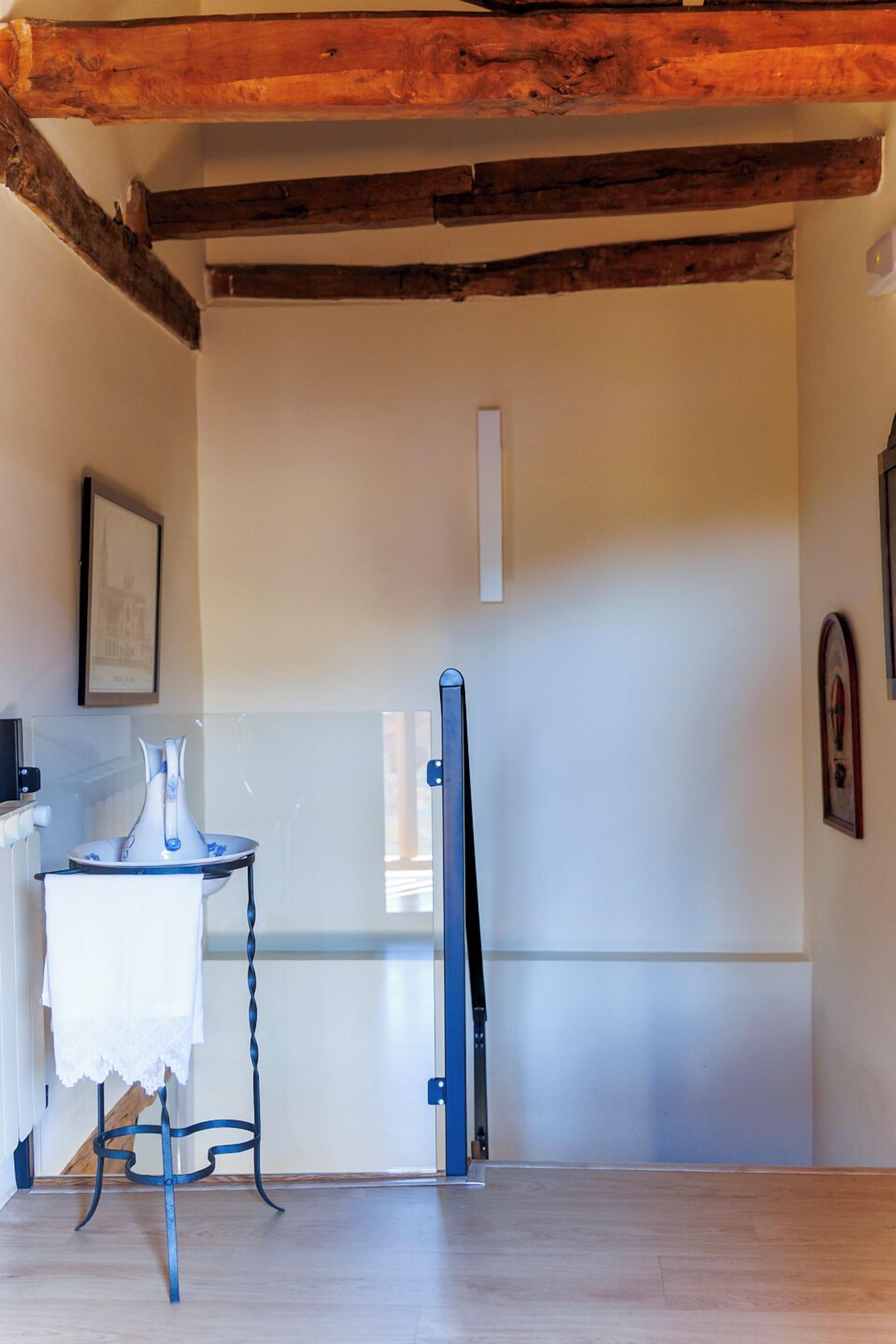 Een kamer met een houten plafond, een witte deur, een klein tafeltje met een wit tafelkleed en een lijst met een foto aan de muur.
