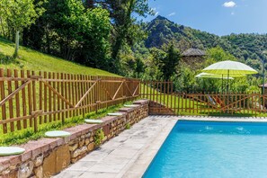 Piscina con muro de piedra y cerca de madera, rodeada de exuberante vegetación y montañas al fondo.