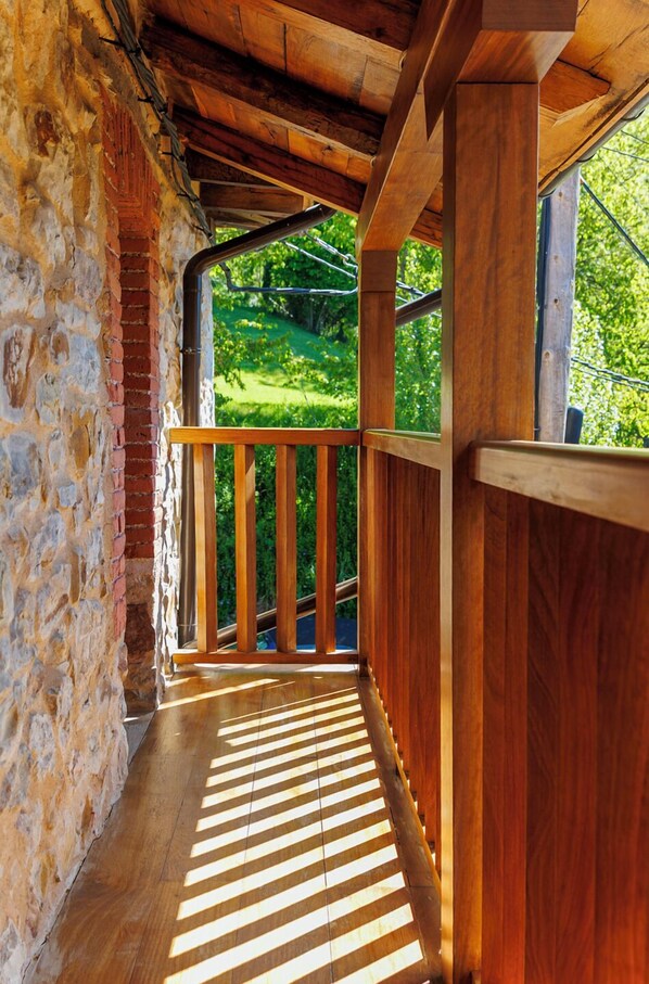 A wooden balcony with a stone wall and a view of a green landscape. - La Casita de Verdiago (Cremenes)