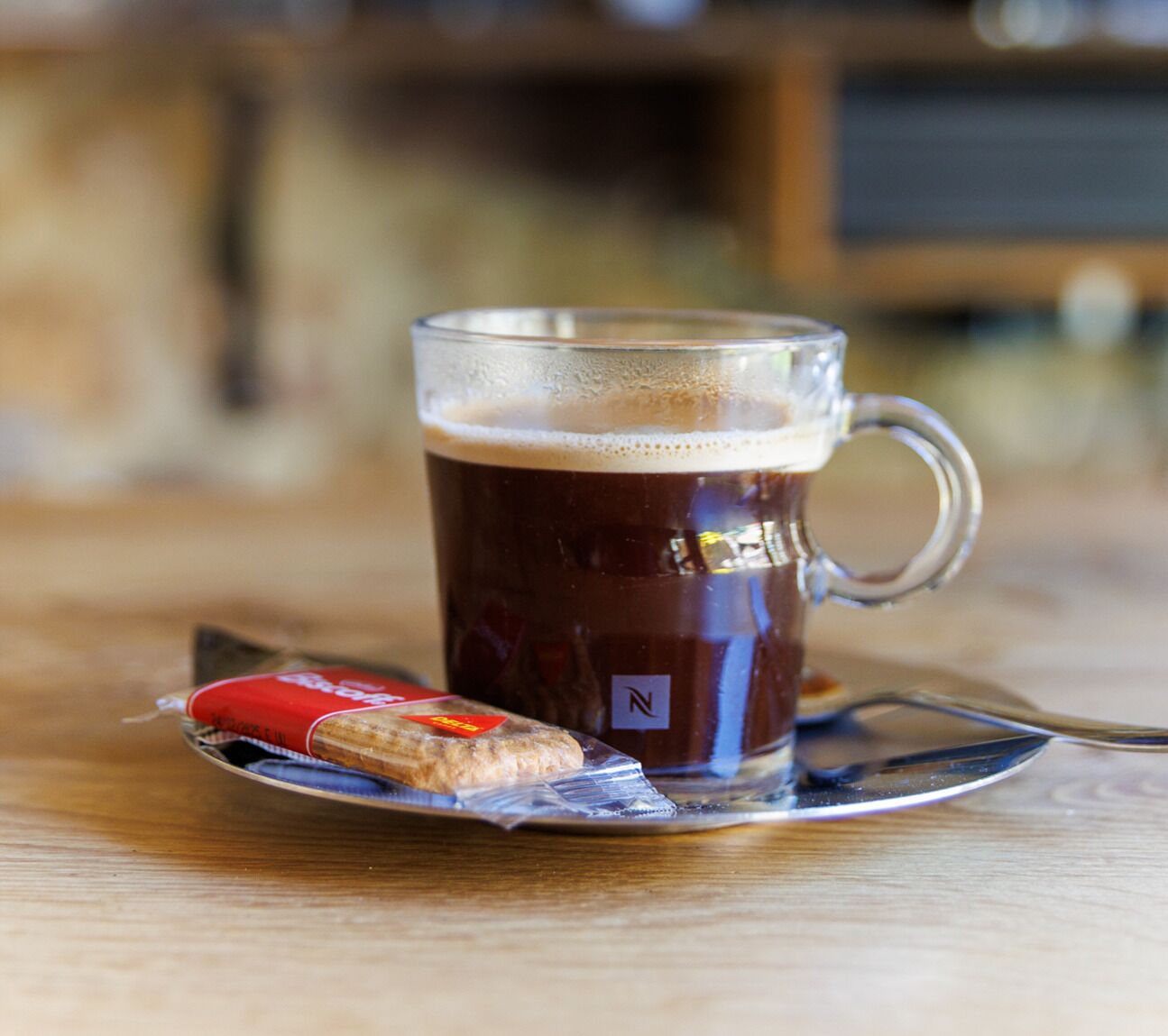 A clear glass mug with a handle, filled with a dark liquid, possibly coffee, on a wooden table.