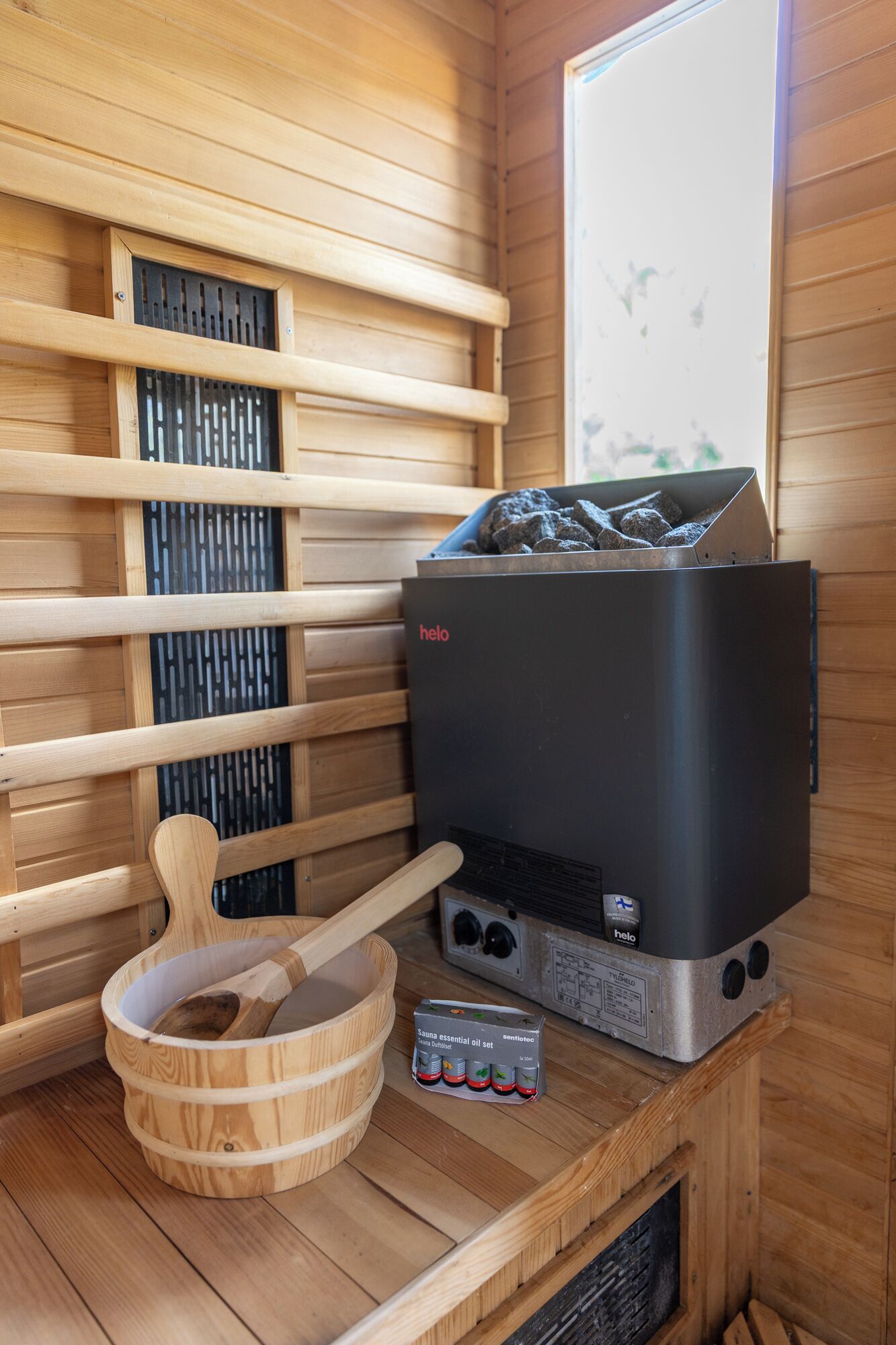 A sauna with a wooden interior, a black heater, and a set of essential oils.