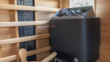 A sauna with a wooden interior, a black heater, and a set of essential oils.