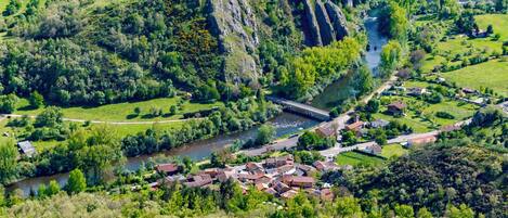 A small village with houses along a river, surrounded by greenery and hills.
