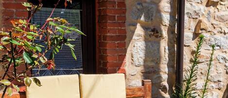 A stone wall, a wooden bench, and a table with a vase of flowers.