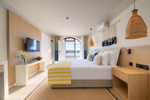 A modern hotel room with a large bed, a TV, a desk, and a view of the outdoors.