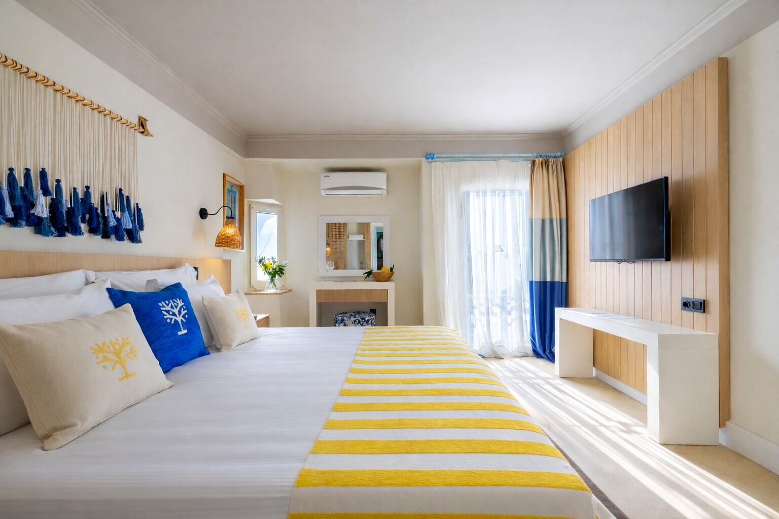 A hotel room with a bed, a TV, a desk, and a window with curtains.