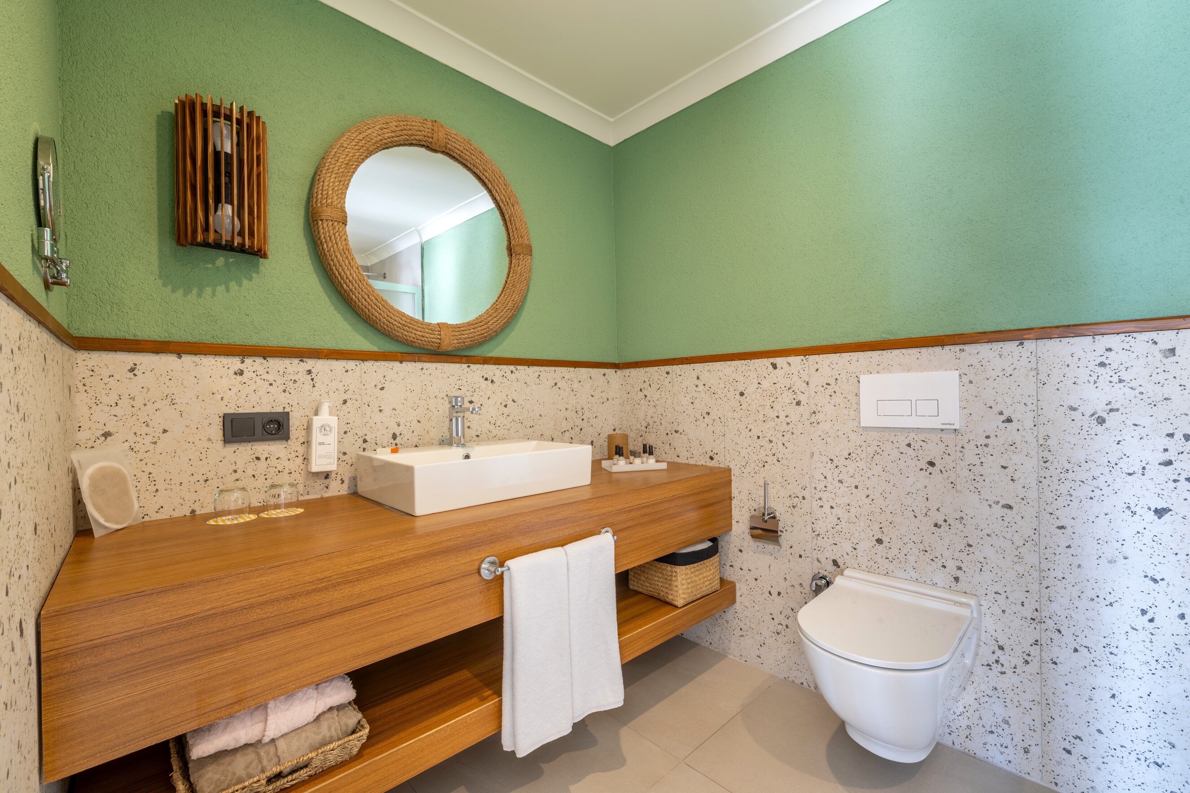 A bathroom with a wooden vanity, a round mirror, a white sink, a toilet, and a towel rack.