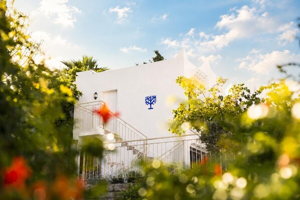 A white building with a blue symbol, surrounded by greenery. - Başka Resort Bodrum (Bodrum)