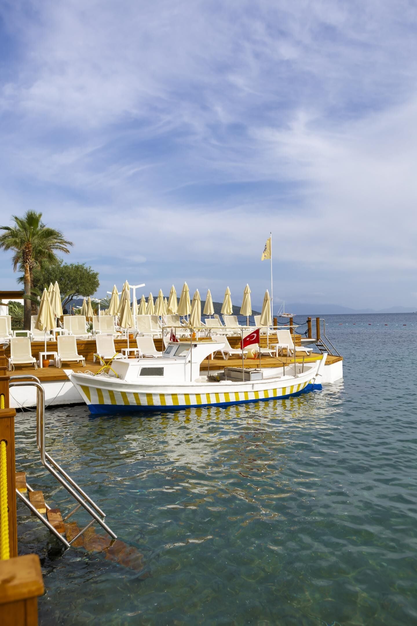 A boat with a flag, clear water, and a deck with lounge chairs and umbrellas.