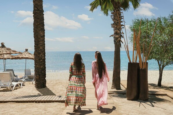 A beach with palm trees, lounge chairs, and a wooden deck. - BaÅŸka Resort Bodrum - All inclusive (Bodrum)